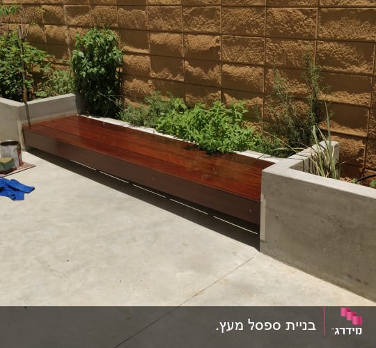 ספסל עץ ליד ערוגת צמחים עם כלי עבודה